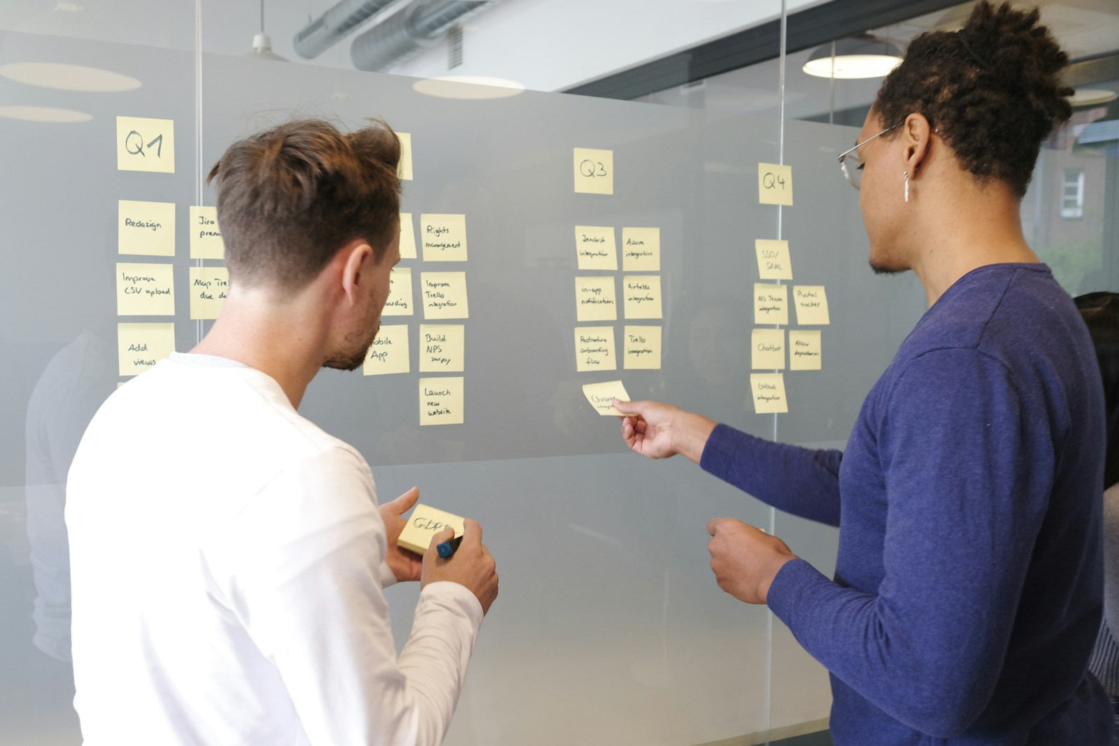 Colleagues co-creating a project plan with notes on a glass wall